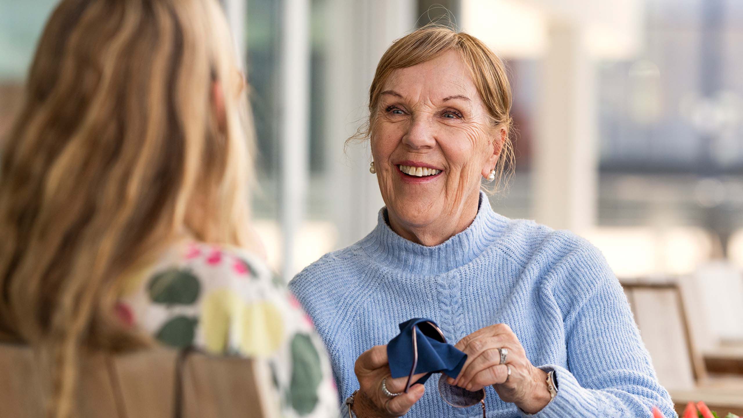 Kaksi naista lounaalla, toinen puhdistaa silm&auml;lasejaan